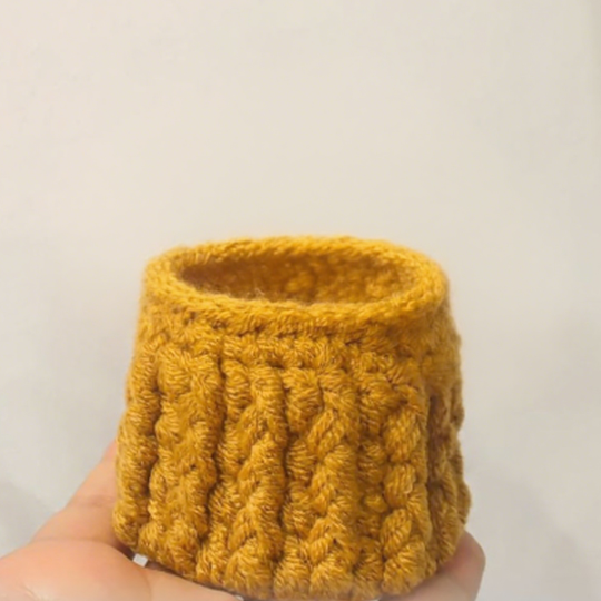 Yellow knitted cup held by a hand against a plain background