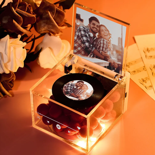 Decorative vinyl record player with a transparent case displaying a couple's photo on an orange surface.