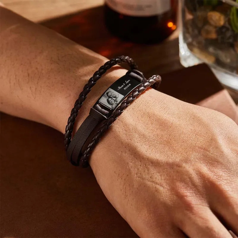 Close-up of a wrist wearing a black braided leather bracelet with a watch face on a wooden surface.