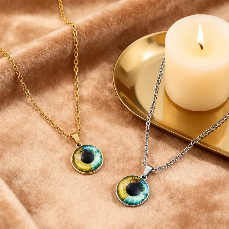Two eye-shaped pendants on gold and silver chains with a candle in the background.