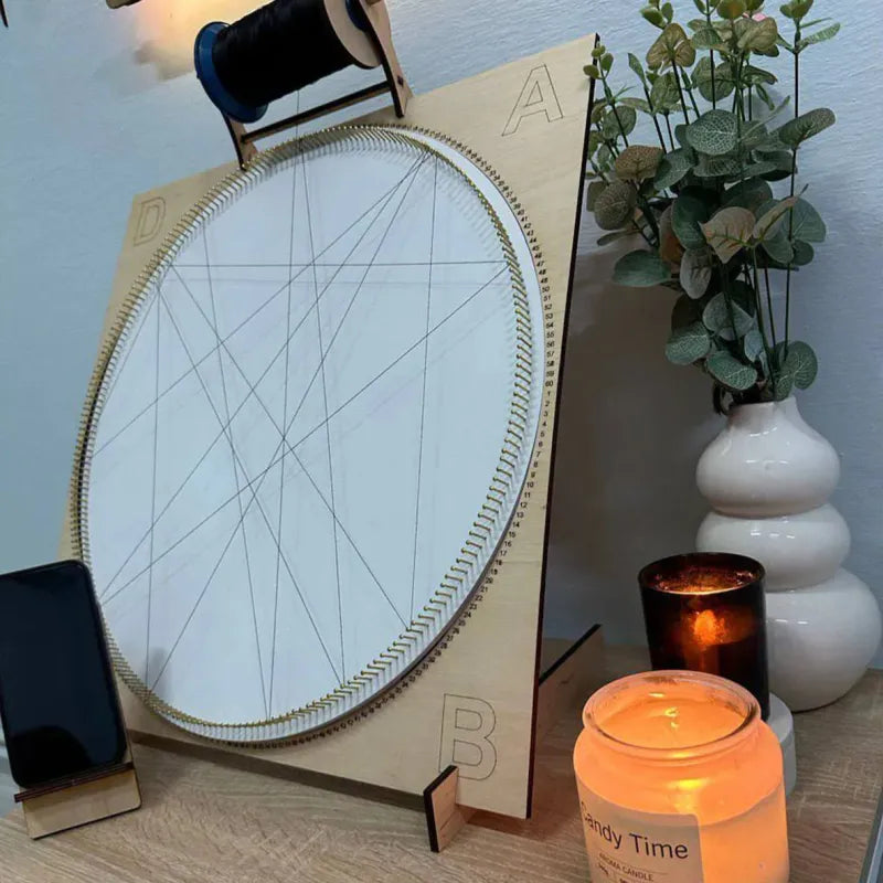 Wooden circular frame with string art on a table next to a candle and plant.