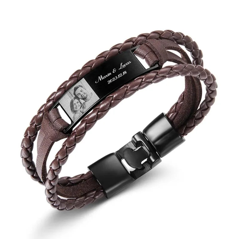 Brown braided leather bracelet with black metal clasp and engraved tag on a white background