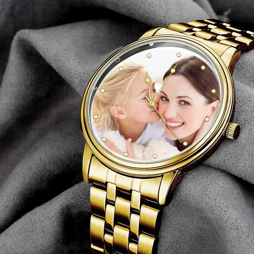 Gold watch with a photo of two people on the face, placed on gray fabric.
