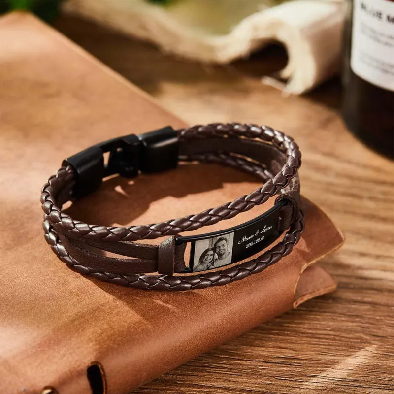 Brown braided leather bracelet with engraved tag on a brown leather surface
