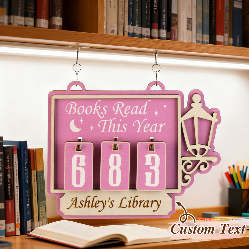 Pink bookshelf tracker with 'Books Read This Year' text, hanging on a bookshelf with books and stationery.