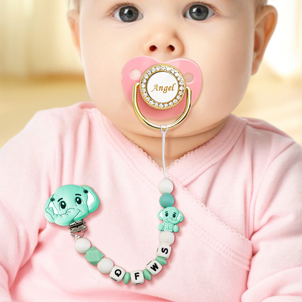 Baby wearing a pink pacifier with a decorative holder, set against a blurred background.