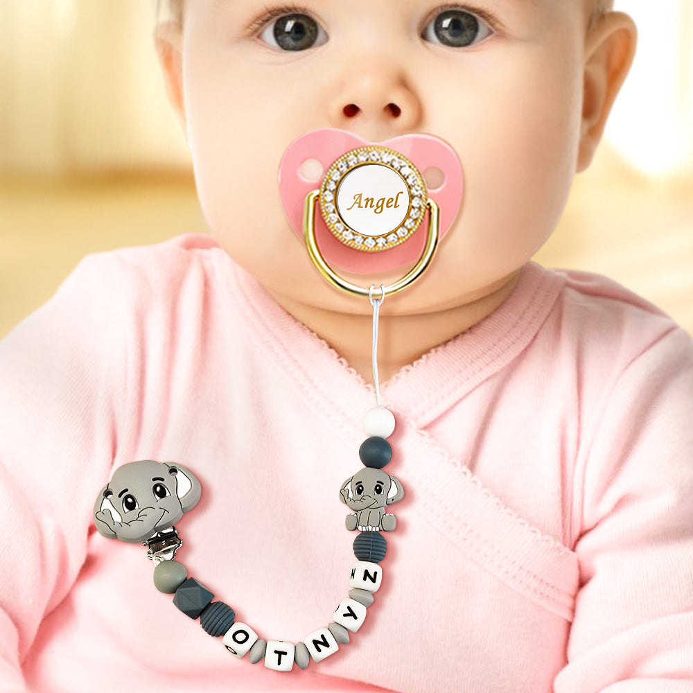 Baby wearing a pink pacifier with a decorative holder, sitting against a blurred background.