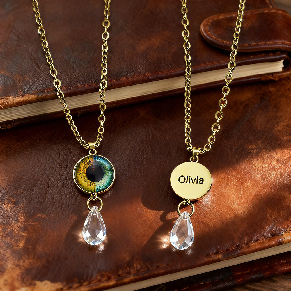 Two gold necklaces with eye-shaped and circular pendants on a brown leather surface.