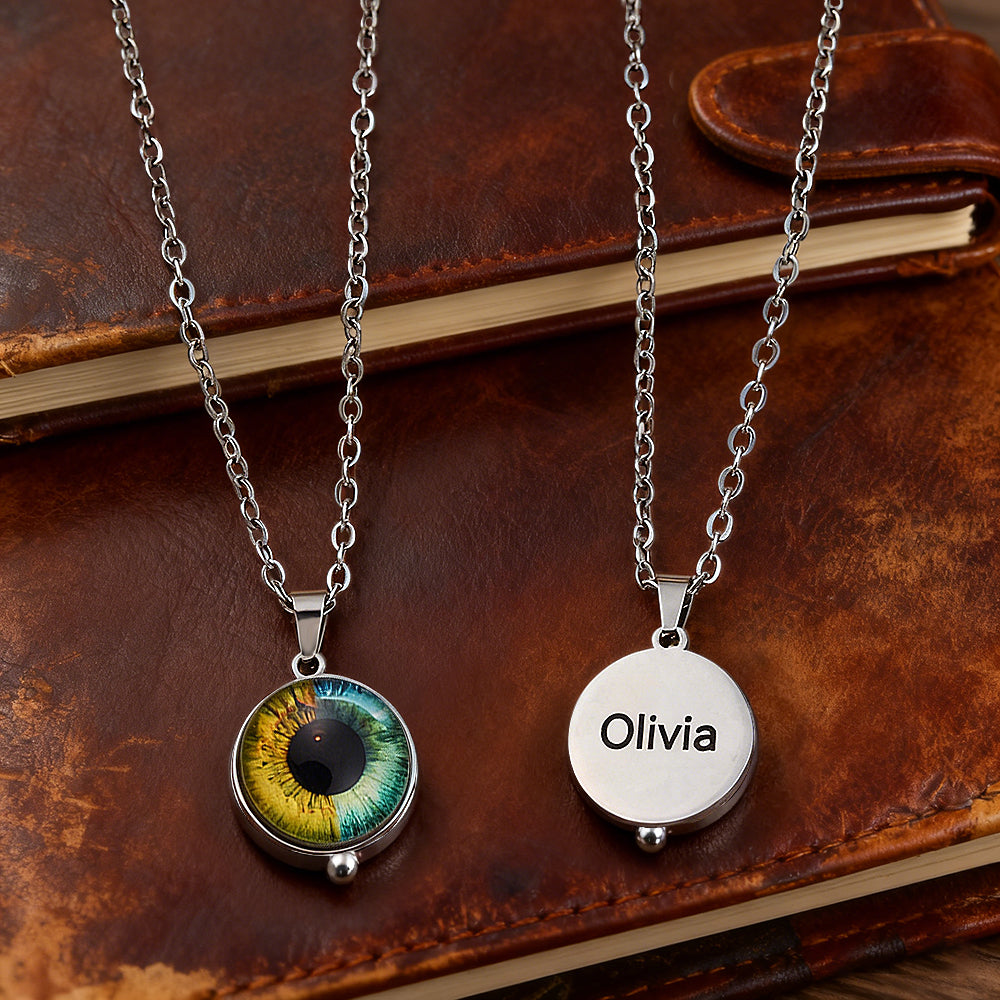 Two silver necklaces with eye-shaped and engraved 'Olivia' pendants on a leather surface.