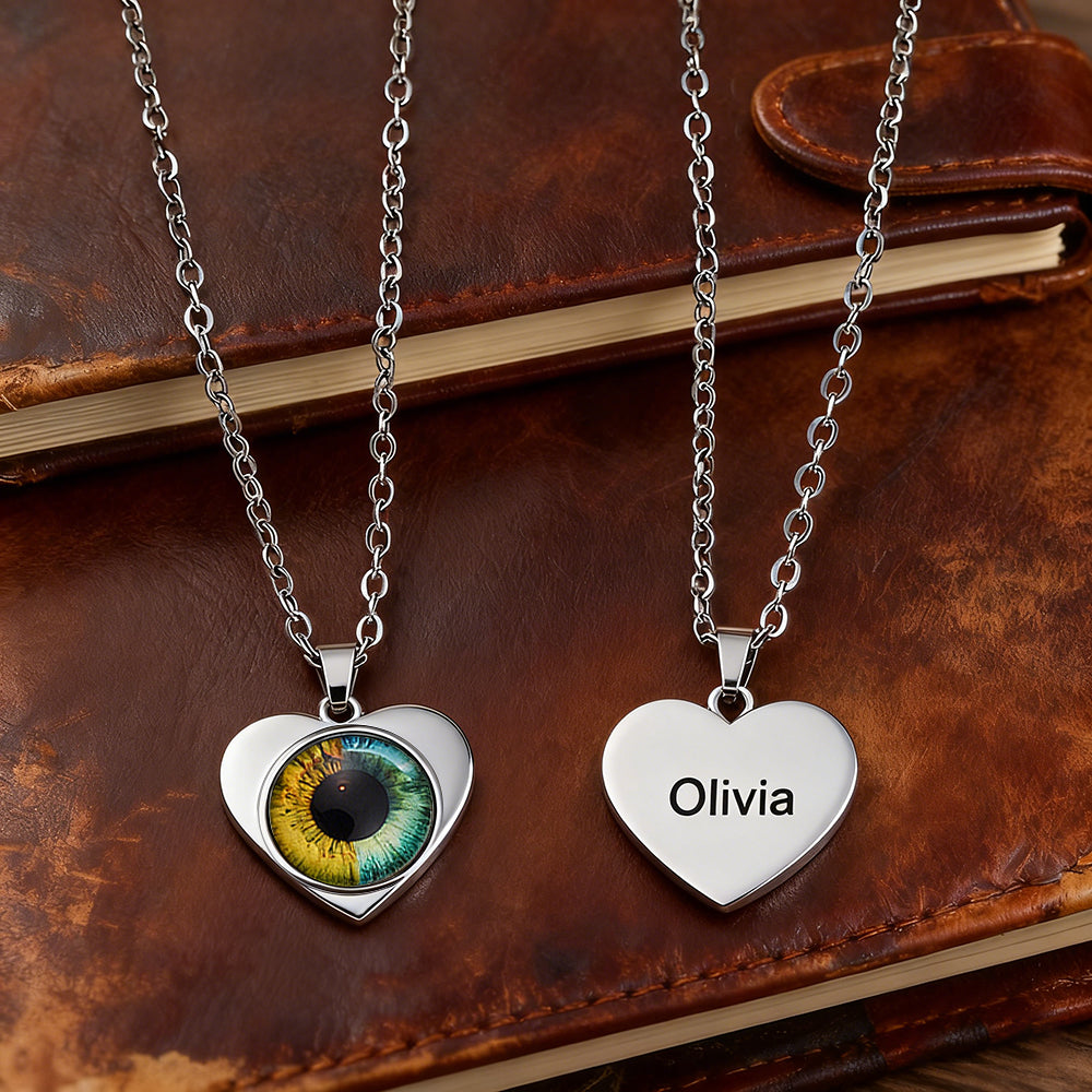 Two heart-shaped pendants on silver chains with one featuring a colorful eye design and the other displaying the name 'Olivia'.