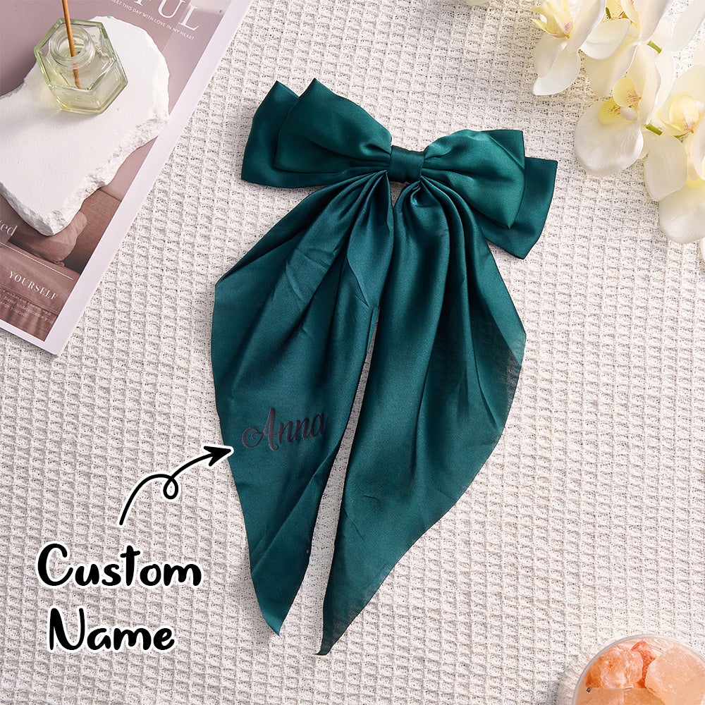 Teal satin scarf with 'Anna' embroidered on it, placed on a textured surface with flowers and a magazine.