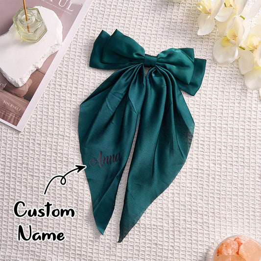 Teal satin scarf with 'Anna' embroidered on it, placed on a textured surface with flowers and a magazine.