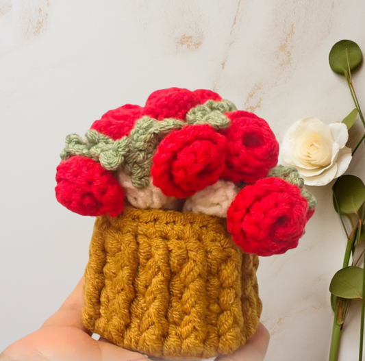 Handmade crochet flower pot with red flowers and green leaves on a light background