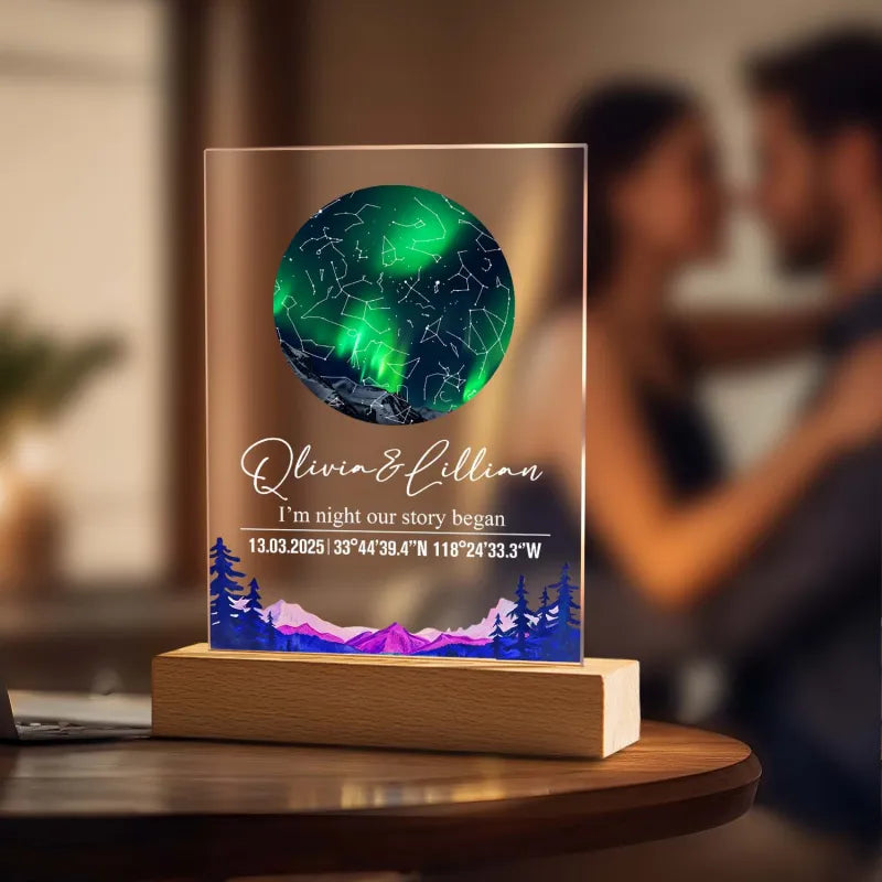 Personalised night light with green and blue design on a wooden base, blurred background of people embracing.